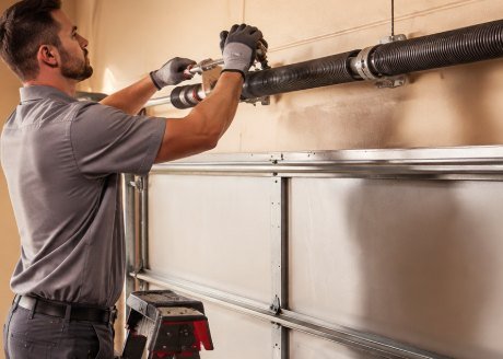 Technician replacing a torsion spring above a residential garage door